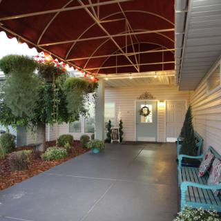 A cozy porch with a canopy, decorated door, and seating area surrounded by plants.