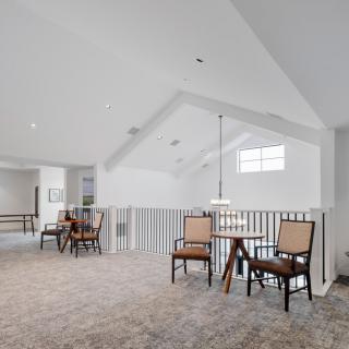 A spacious and bright loft area with seating and a table, featuring carpeted flooring and white railings.