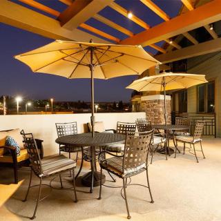 A cozy outdoor patio area with tables, chairs, and umbrellas, warmly lit in the evening.