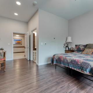 A cozy bedroom with wooden flooring, a patterned bedspread, and soft lighting.