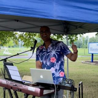 A musician performing outdoors under a tent with a keyboard and microphone.