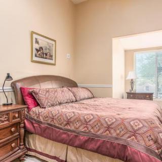 A cozy bedroom featuring a patterned bedspread, bedside lamp, and bright window.