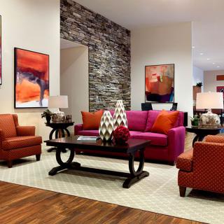 A modern living room featuring a vibrant color scheme with orange and pink seating, complemented by abstract artwork and a stacked stone accent wall.