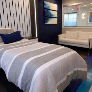 A modern bedroom with a striped bedspread, decorative pillows, artwork on the walls, and a white sofa.