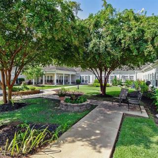 A lush garden with a pathway lined by trees and benches, offering a serene outdoor space.