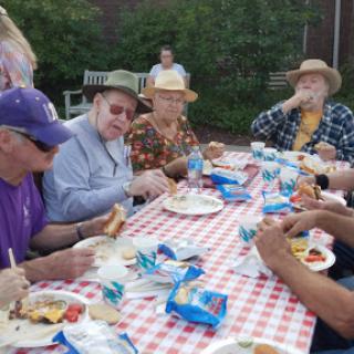 A cheerful outdoor gathering where senior citizens enjoy a meal together, surrounded by nature.