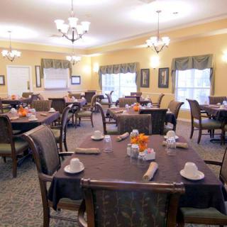 An elegantly set dining room with multiple tables and chairs, featuring chandeliers and neatly arranged table settings.