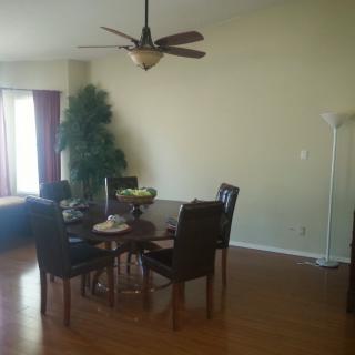 A cozy dining area with a round table and chairs on a hardwood floor, featuring a ceiling fan and a decorative plant.