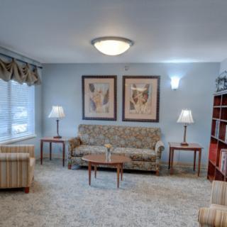 A cozy living room featuring a patterned sofa, armchairs, coffee table, and floor lamps with artwork on the wall.