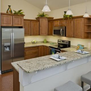 A modern kitchen with wooden cabinets and a granite countertop, featuring stainless steel appliances and pendant lighting.