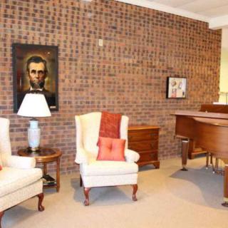 A cozy living room featuring a brick wall, two armchairs, a grand piano, and decorative artwork.