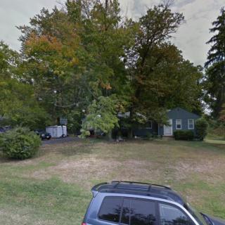 A suburban yard with a house surrounded by trees and a car parked in front.