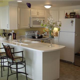 A modern kitchen featuring white cabinets, a large countertop with bar stools, and decorative flowers.