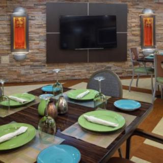 A modern dining room setup with a neatly arranged table featuring green and blue plates, napkins, wine glasses, and a wall-mounted TV.