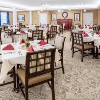 An elegantly set dining area with neatly arranged tables and chairs, featuring red napkins and a cozy atmosphere.