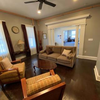 A cozy living room with a sofa, two armchairs, and a coffee table, featuring hardwood floors and a ceiling fan.