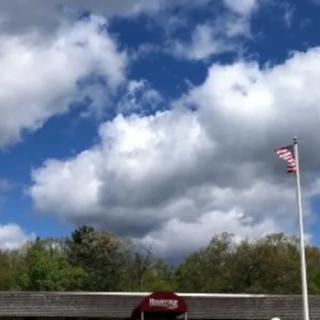 A scenic view of clouds in a blue sky above a building and an American flag.