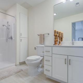 A clean and modern bathroom featuring a shower, toilet, sink with a large mirror, and white cabinetry.
