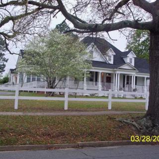 A picturesque house with a wrap-around porch, surrounded by trees and a white fence.