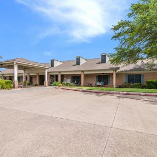 A wide-angle view of a building with a large driveway and surrounding greenery under a clear blue sky.