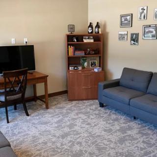 A cozy living room with a sofa, desk, bookshelf, and a television.