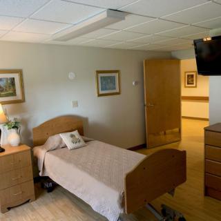 A cozy bedroom with a single bed, television, and decorative paintings on the wall.