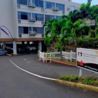 Entrance of a hospital building with palm trees and signage.