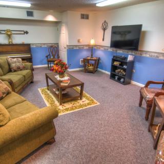 A cozy living room with a large green sofa, a TV mounted on the wall, and a coffee table in the center.