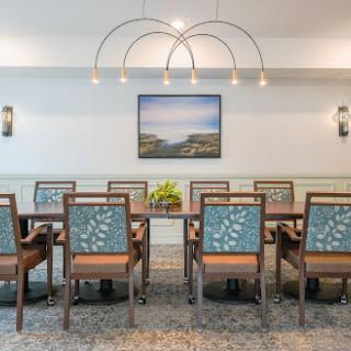A modern dining space featuring a large table with stylish chairs, complemented by elegant lighting and a serene artwork on the wall.