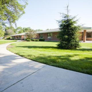 A scenic view of a building surrounded by lush green lawns and trees, with a curving sidewalk in the foreground.