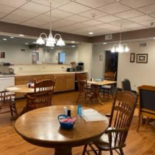 A cozy dining area with wooden tables and chairs, softly illuminated by overhead lights.