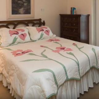 A cozy bedroom featuring a bed with a floral quilt and matching pillows, beside a wooden chest of drawers.