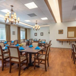 A spacious dining room with elegant chandeliers and neatly arranged tables set with blue napkins.