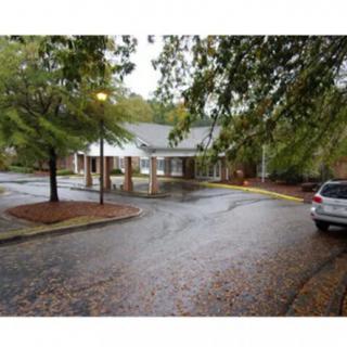 A building entrance with a driveway, surrounded by trees on an overcast day.