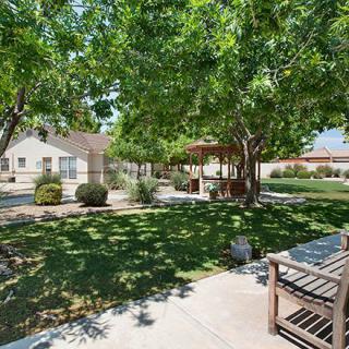 A serene park setting with lush trees, a gazebo, and benches along a paved pathway.