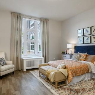 A cozy, modern bedroom featuring a large window, artwork above the bed, and warm-toned furnishings.