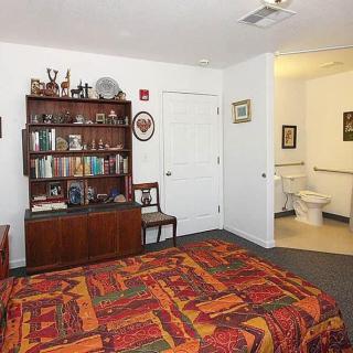 A cozy bedroom featuring a colorful bedspread, a wooden bookshelf filled with books and decorations, and an adjoining bathroom.