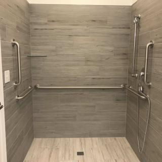 A modern, accessible shower with grab bars and tiled walls.