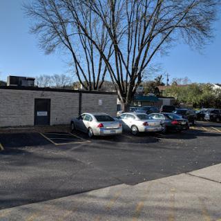 A view of a parking lot with several vehicles parked, accompanied by a tall tree and a clear blue sky.