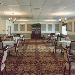A spacious dining room with neatly arranged tables and chairs, illuminated by chandeliers.
