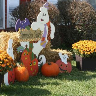 Festive Halloween display with ghosts, pumpkins, and hay bales surrounded by autumn flowers.