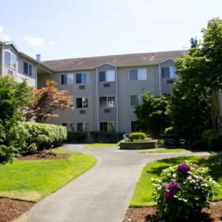 A sunny view of a residential apartment building with a landscaped pathway and greenery.