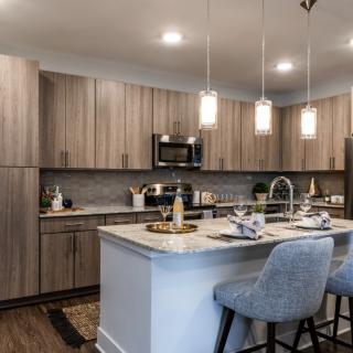 A modern kitchen with an island counter and wooden cabinets, featuring pendant lights and bar stools.