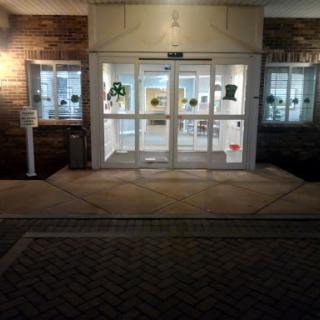 The entrance of a building illuminated at night, showcasing its glass doors and decorative plants.