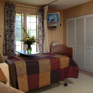A cozy room with a hospital bed, floral curtains, and a small TV mounted on the wall.