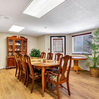 A spacious dining room with a wooden table and chairs, surrounded by indoor plants and natural lighting.