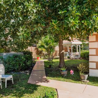 A tranquil garden with a pathway leading to a gazebo surrounded by lush greenery and outdoor seating.