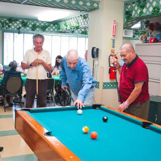 A group of elderly men enjoying a game of billiards at a recreation center.
