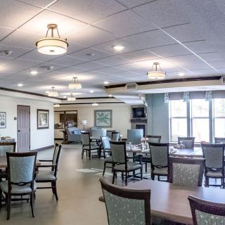 A spacious dining room with neatly arranged tables and chairs, featuring elegant lighting fixtures and large windows providing natural light.