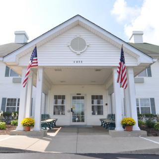 A white building entrance with two American flags and flower pots on each side.